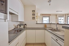 Una cocina moderna con armarios blancos, un lavamanos de acero inoxidable y un lavavajillas.
