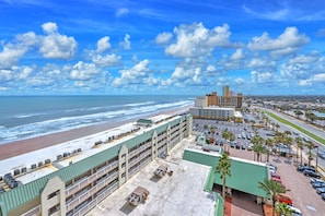 A hotel with a beach view, multiple floors, and a parking lot with cars and palm trees. - Oceanview | Private Balcony | Pool | Hot Tub (Daytona Beach)
