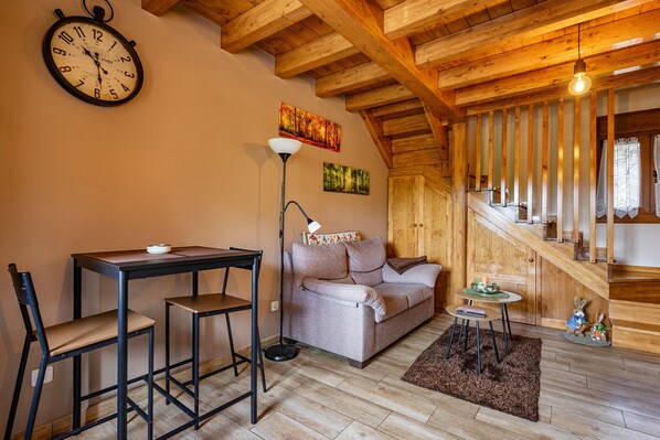 Un salon chaleureux avec un plafond en bois, un canapé, une table avec des chaises, une horloge et des œuvres d’art accrochées au mur.