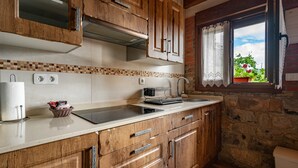 Cocina con alacenas de madera, una encimera, un ventanal con cortinas y vista a follaje exterior.