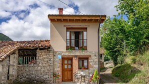 Una casa de piedra de dos pisos con techo de tejas, una puerta de madera y un pequeño balcón con plantas en macetas.