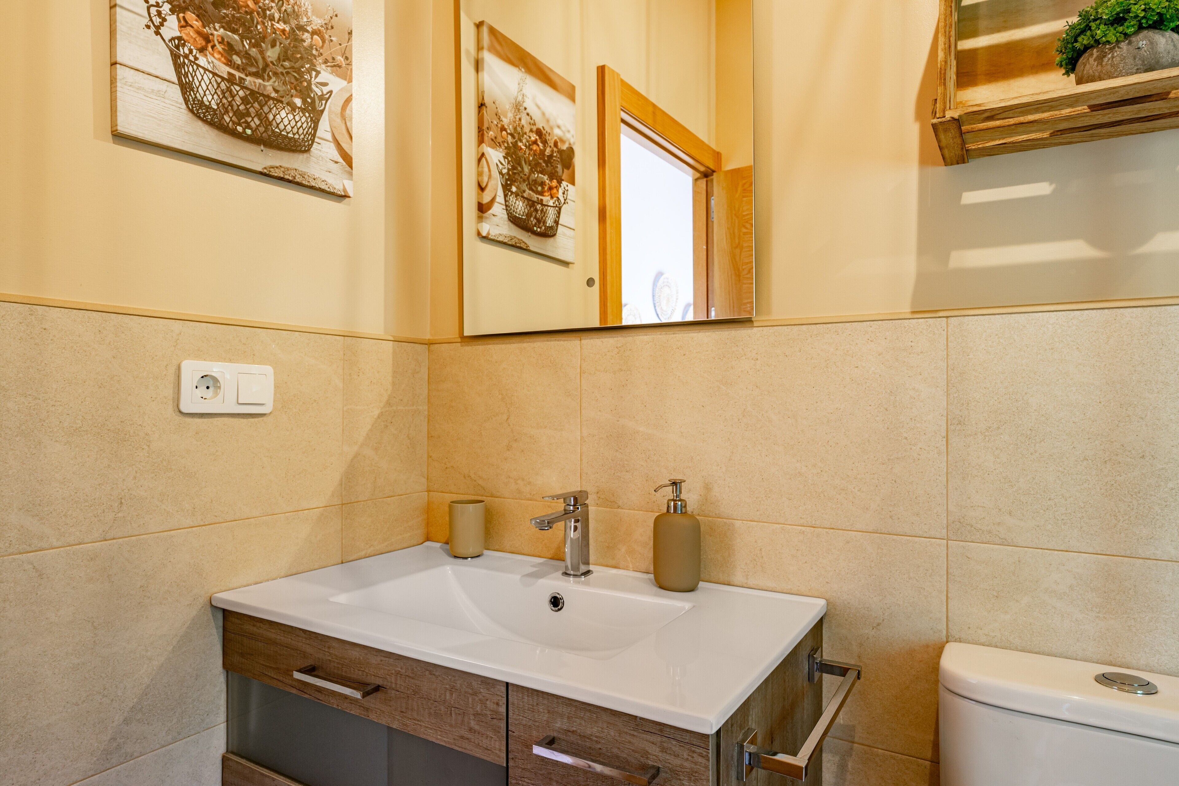 A bathroom with a white sink, wooden cabinet, and a toilet.