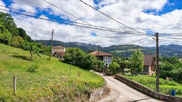 A rural road with houses, a stone wall, and mountains in the background.