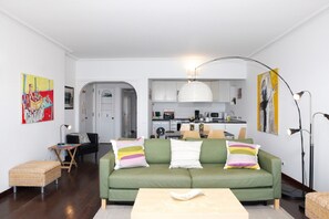 Ein Wohnzimmer mit einem grünen Sofa, einem kleinen Tisch und einer Küche im Hintergrund.