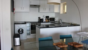 A modern kitchen with white cabinets, a washing machine, a microwave, and a glass dining table with chairs. - Apartment 'Cascais Bay Terrace V' with Sea View, Wi-Fi and Air Conditioning (Cascais)
