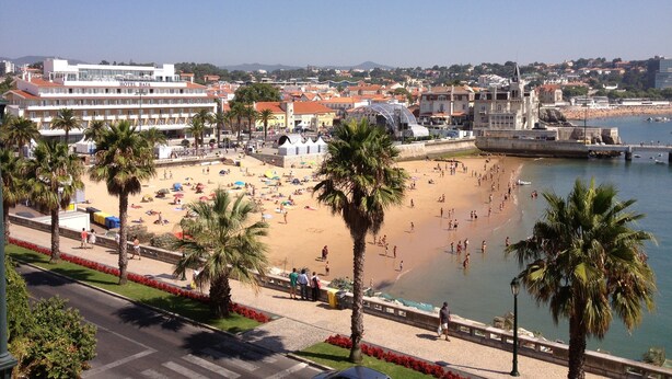 A coastal cityscape with a beach, palm trees, and a hotel named 'HOTEL RATA' in the background. - Apartment 'Cascais Bay Terrace V' with Sea View, Wi-Fi and Air Conditioning (Cascais)
