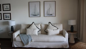 A living room with a sofa, two framed pictures, two side tables with lamps, and a wall-mounted air conditioner. - Apartment 'Cascais Bay Terrace V' with Sea View, Wi-Fi and Air Conditioning (Cascais)