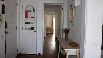 Un corridoio con una porta bianca, un tavolo di legno con un vaso e uno specchio appeso al muro.