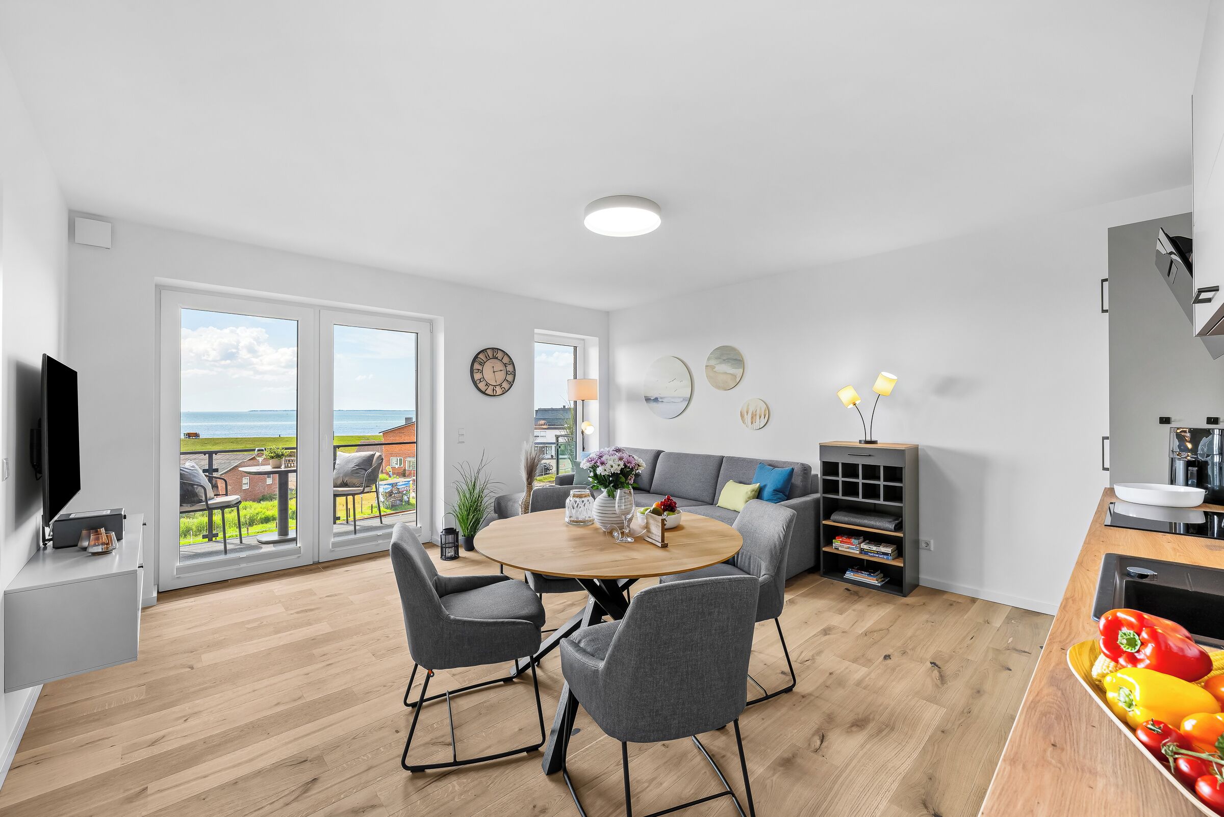 A modern living room with a dining area, large windows, and a view of the sea.