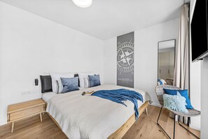 Ein modernes Schlafzimmer mit einem großen Bett, einem an der Wand befestigten Fernseher und einem hölzernen Nachttisch.