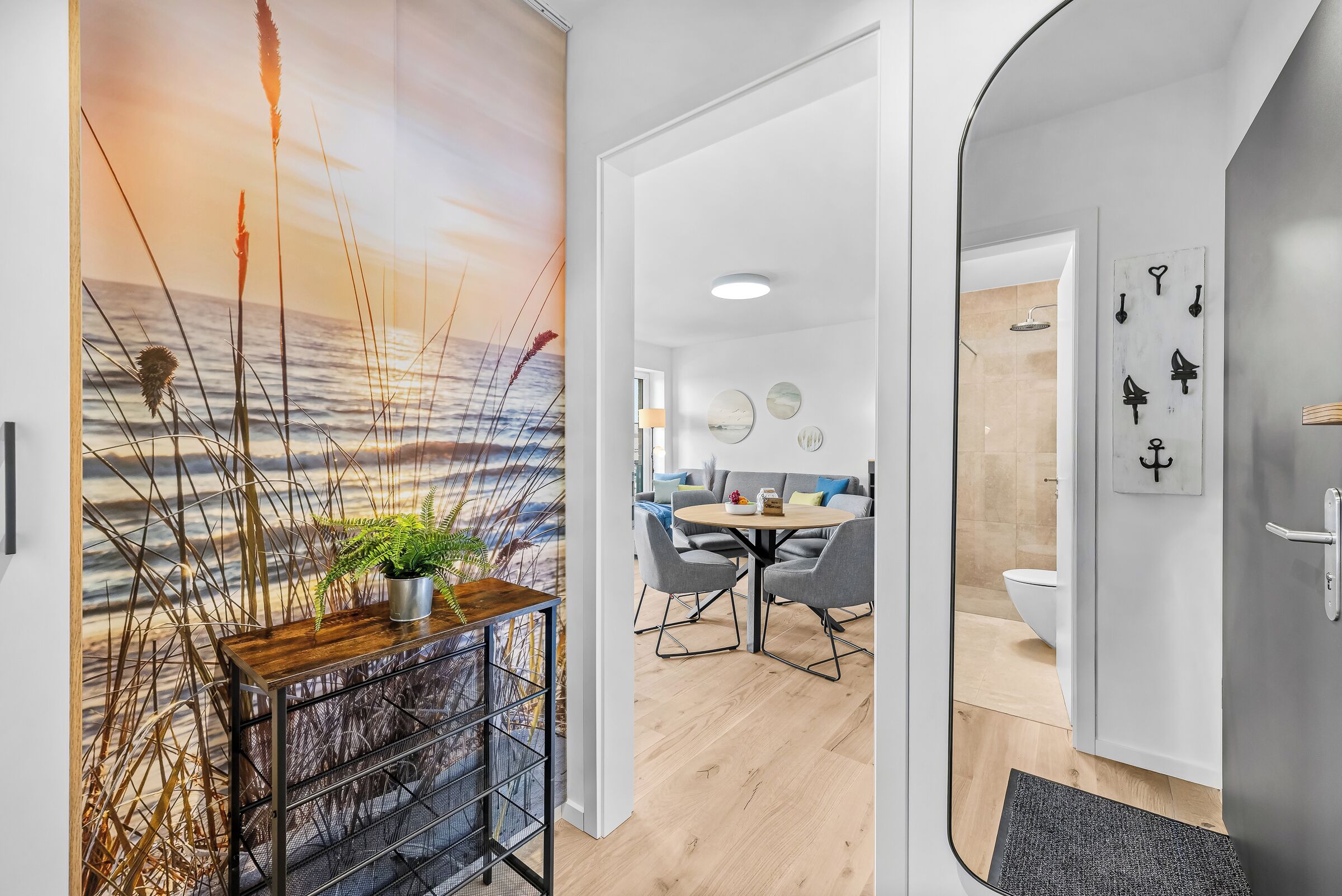 Un intérieur moderne avec un plancher en bois, un coin repas avec une table ronde et des chaises, et une vue sur l’océan par une grande fenêtre.