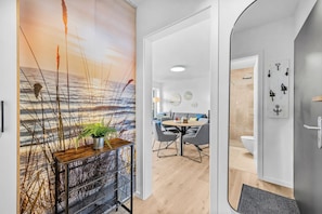 Un intérieur moderne avec un plancher en bois, un coin repas avec une table ronde et des chaises, et une vue sur l’océan par une grande fenêtre.