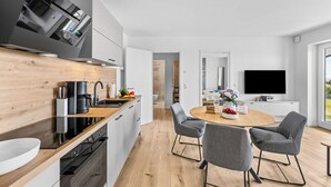 A modern kitchen with a built-in Bosch range hood, a coffee machine, and a dining area with a round table and grey chairs. - The View B16 Meeresleuchten - Balcony, Sofa bed, shared Sauna, Elevator (Dagebüll)
