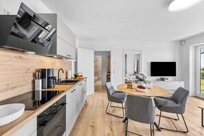 Eine moderne Küche mit Bosch-Dunstabzugshaube, einer Kaffeemaschine und einem Essbereich mit rundem Tisch und grauen Stühlen.