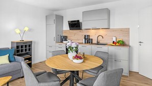 A modern kitchen with a dining area, grey furniture, and a wooden table with a fruit bowl and flowers. - The View B16 Meeresleuchten - Balcony, Sofa bed, shared Sauna, Elevator (Dagebüll)