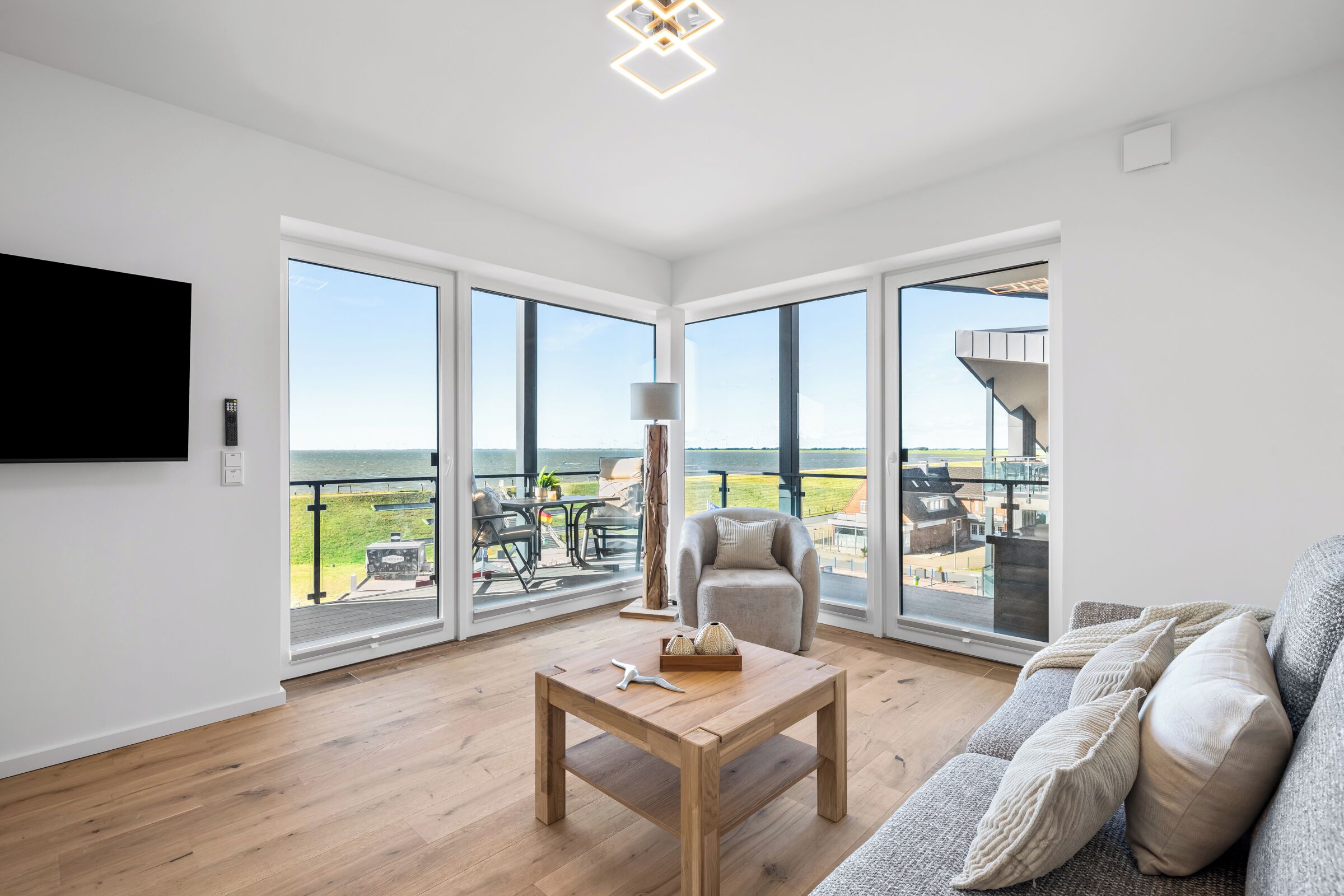 Een ruime woonkamer met een houten vloer, een bank, een salontafel en grote ramen met uitzicht op de omgeving.