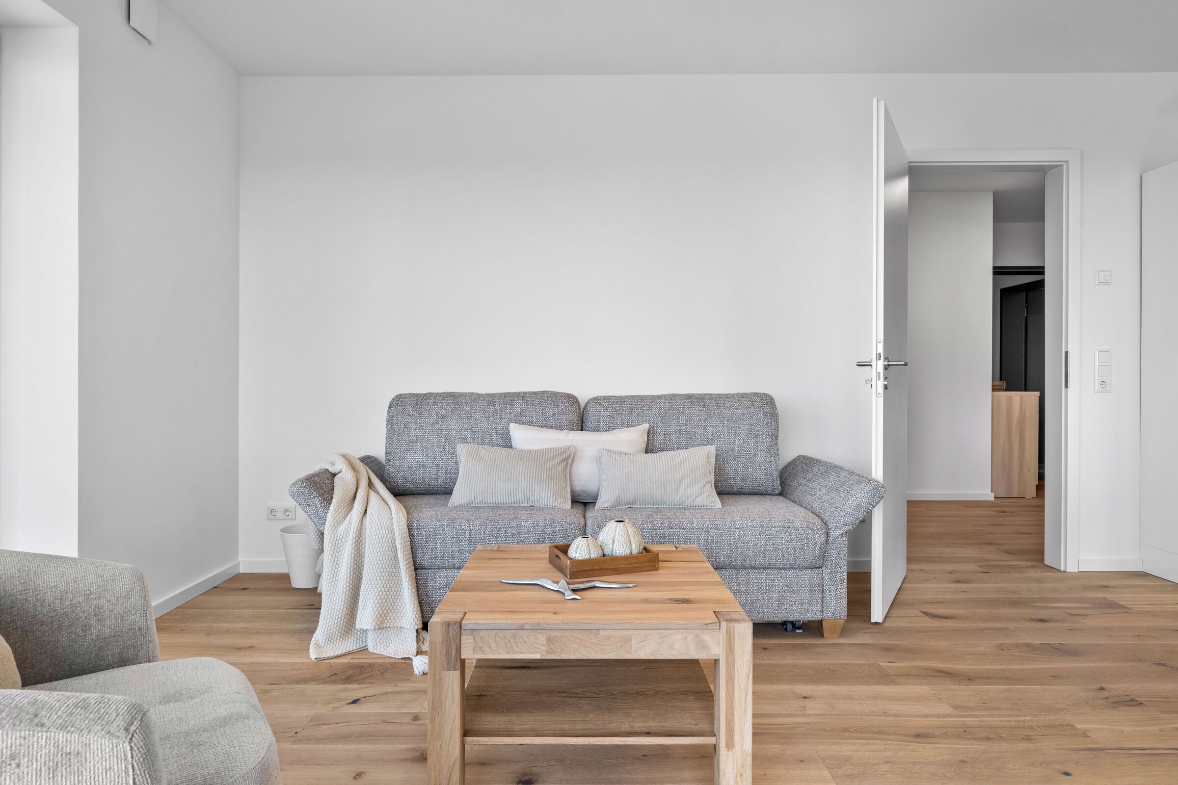 En minimalistisk stue med en grå sofa med mønster, et træbord og en hvid væg.