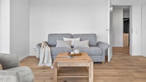 Ein minimalistisches Wohnzimmer mit einem grauen gemusterten Sofa, einem Holztisch und einer weißen Wand.