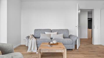 En minimalistisk stue med en grå sofa med mønster, et træbord og en hvid væg.