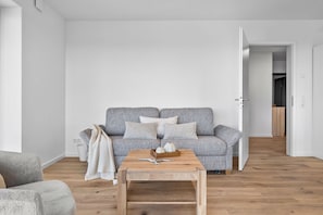 A minimalist living room with a grey patterned sofa, a wooden coffee table, and a white wall. - The View B14 Nordseeperle – Balcony, sea view, shared sauna (Dagebüll)