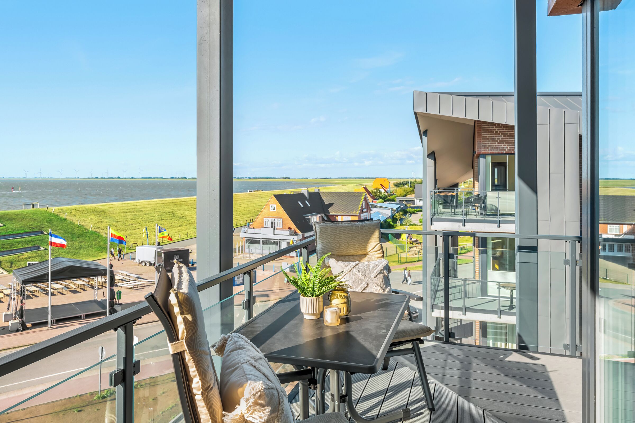 Ein Balkon mit Blick auf einen Fluss und Windkraftanlagen, ausgestattet mit einem Tisch, Stühlen und einem Topfpflanzen.