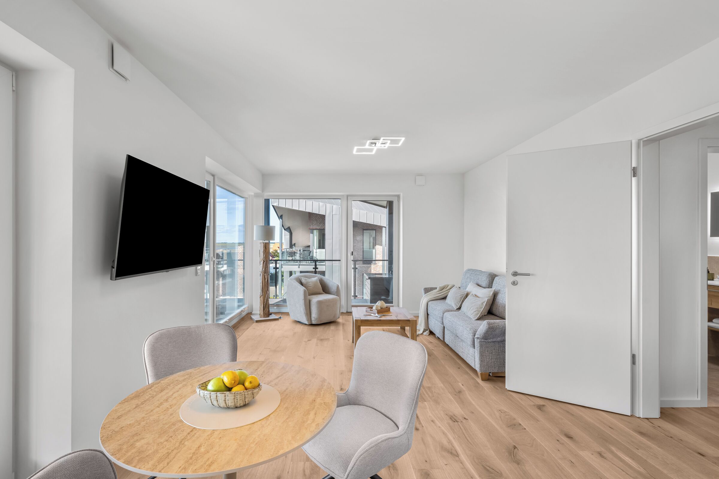 Ein modernes Wohnzimmer mit Essbereich, einem Wand-Fernseher und einem großen Fenster mit Blick auf die Stadt.