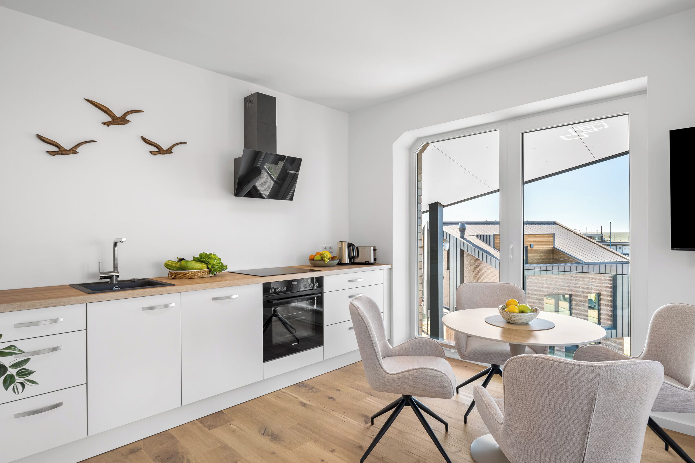 Una cucina moderna con forno integrato, un'area pranzo con tavolo e sedie rotonde, e un'ampia finestra che offre vista sulla città.
