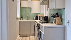 A compact kitchen with white cabinets, a built-in oven, and a countertop with various appliances. - The Red House, 2 Bed Garden Flat in Totterdown, Bristol BS3 4TJ near city centre (Bristol)