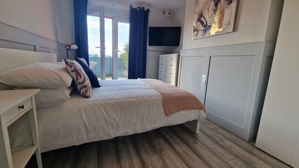 A bedroom with a bed, bedside tables, a TV, and a view of the outdoors. - The Red House, 2 Bed Garden Flat in Totterdown, Bristol BS3 4TJ near city centre (Bristol)