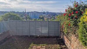 A rooftop garden with a view of a cityscape, including buildings and a church spire. - The Red House, 2 Bed Garden Flat in Totterdown, Bristol BS3 4TJ near city centre (Bristol)