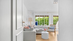 A room with a sofa, a chair, a round table, and a window with a view of greenery.