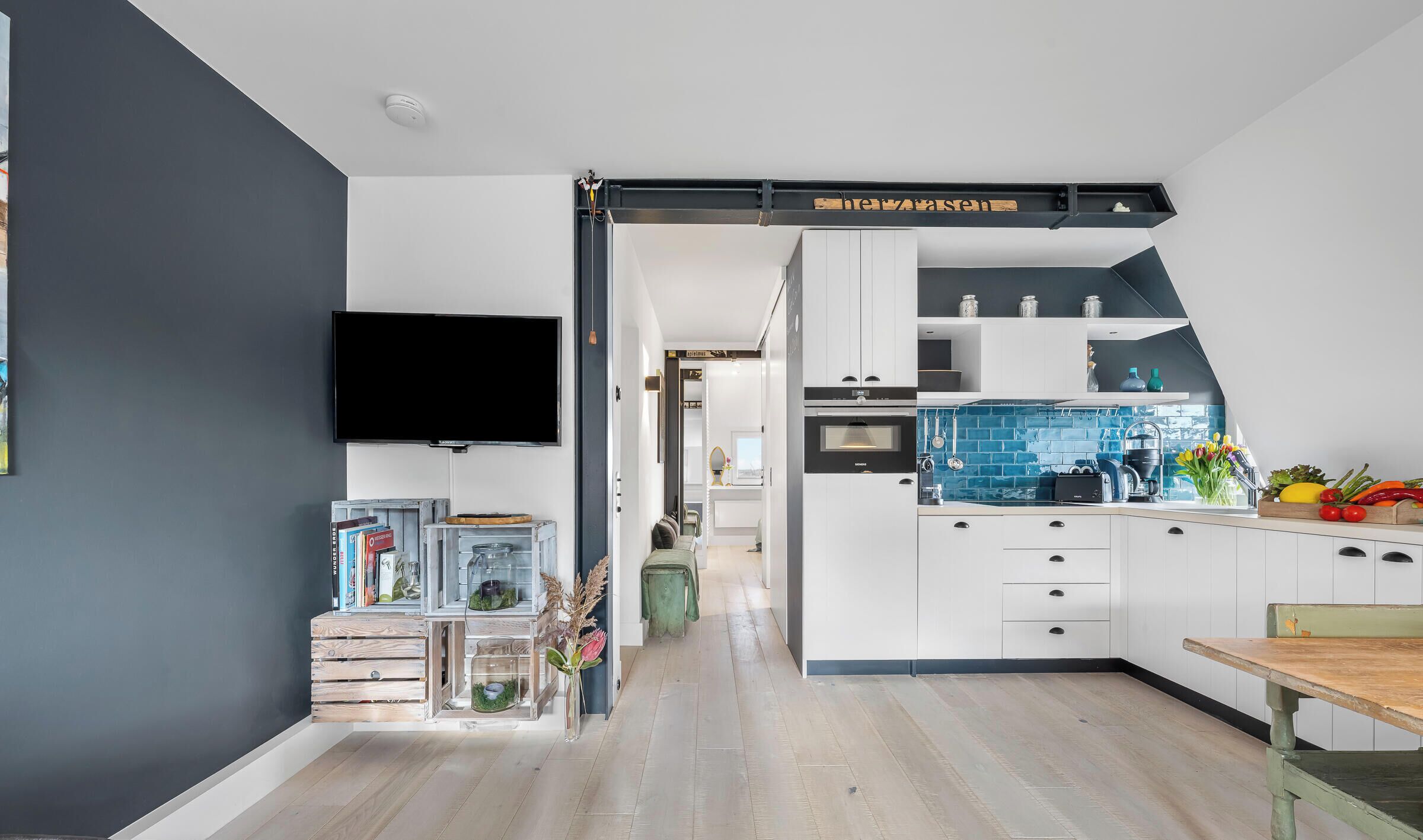 Een moderne keuken met witte kastjes, een blauwe achterwand en een houten eettafel.
