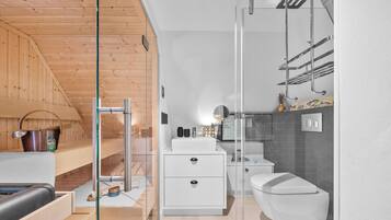 Un baño moderno con cabina de ducha de vidrio, un lavabo blanco y un inodoro.