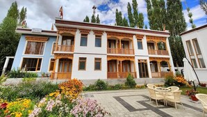 Un hotel de varios pisos con arquitectura tradicional, balcones y un jardín con mobiliario exterior.
