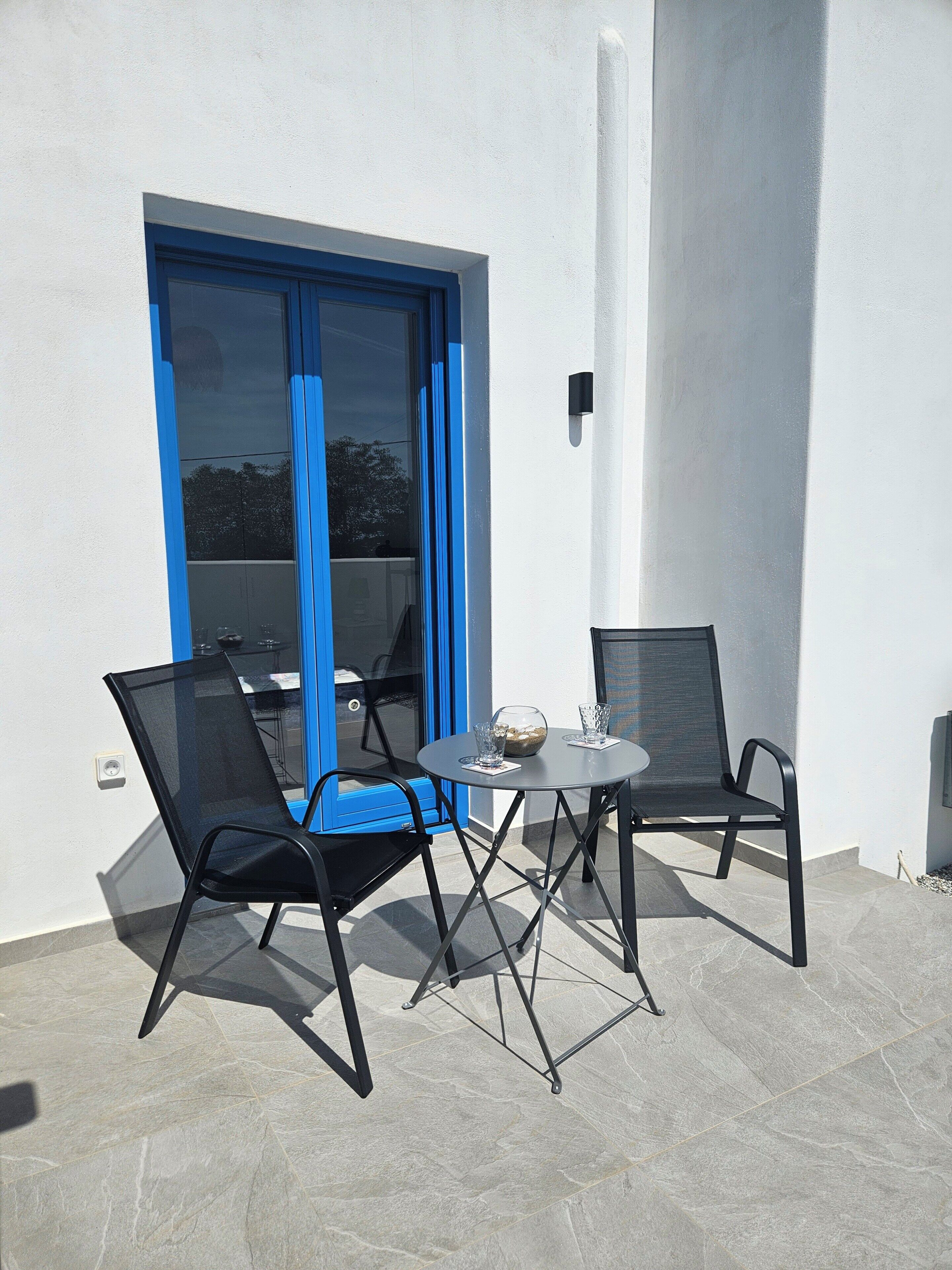 A patio with two chairs and a table, a blue curtain, and a white wall.
