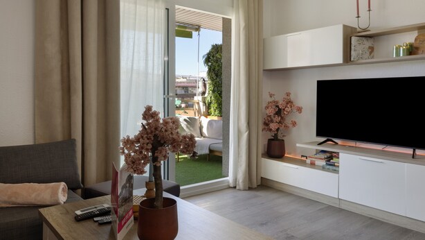 A modern living room with a sofa, a coffee table with remote controls and a book, a TV on a stand, and a sliding glass door leading to an outdoor area. - Holiday Home 'Salou Blueme' with Mountain View, Wi-Fi and Air Conditioning (Salou)