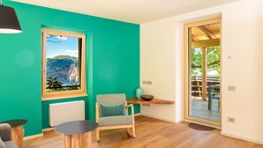 Une pièce avec un plancher en bois, un mur de couleur turquoise, une fenêtre donnant sur les montagnes, une chaise, une table et une porte menant à l’extérieur.