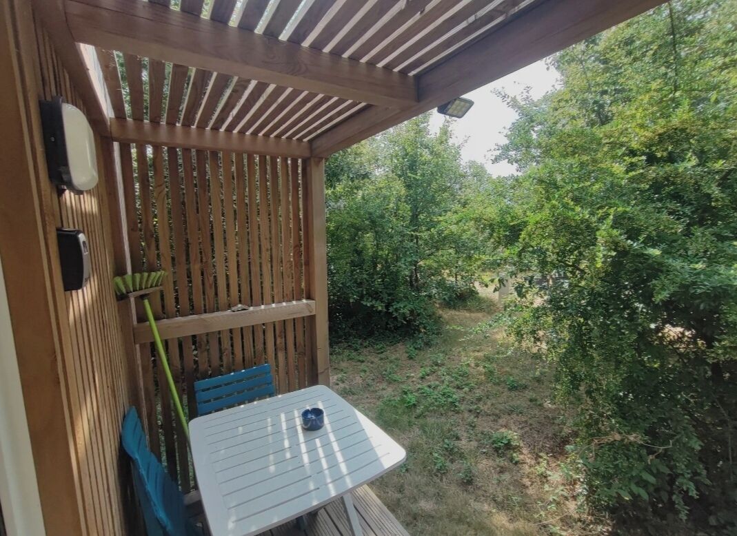 Una terrassa de fusta amb taula i cadires, envoltada de verdura.