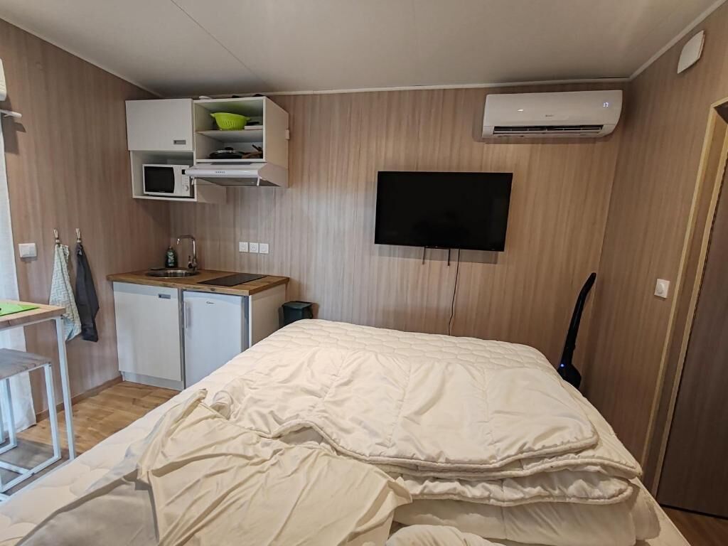 Une chambre d’hôtel de taille réduite, équipée d’un lit, d’une petite kitchenette, d’un téléviseur et d’un appareil de climatisation.