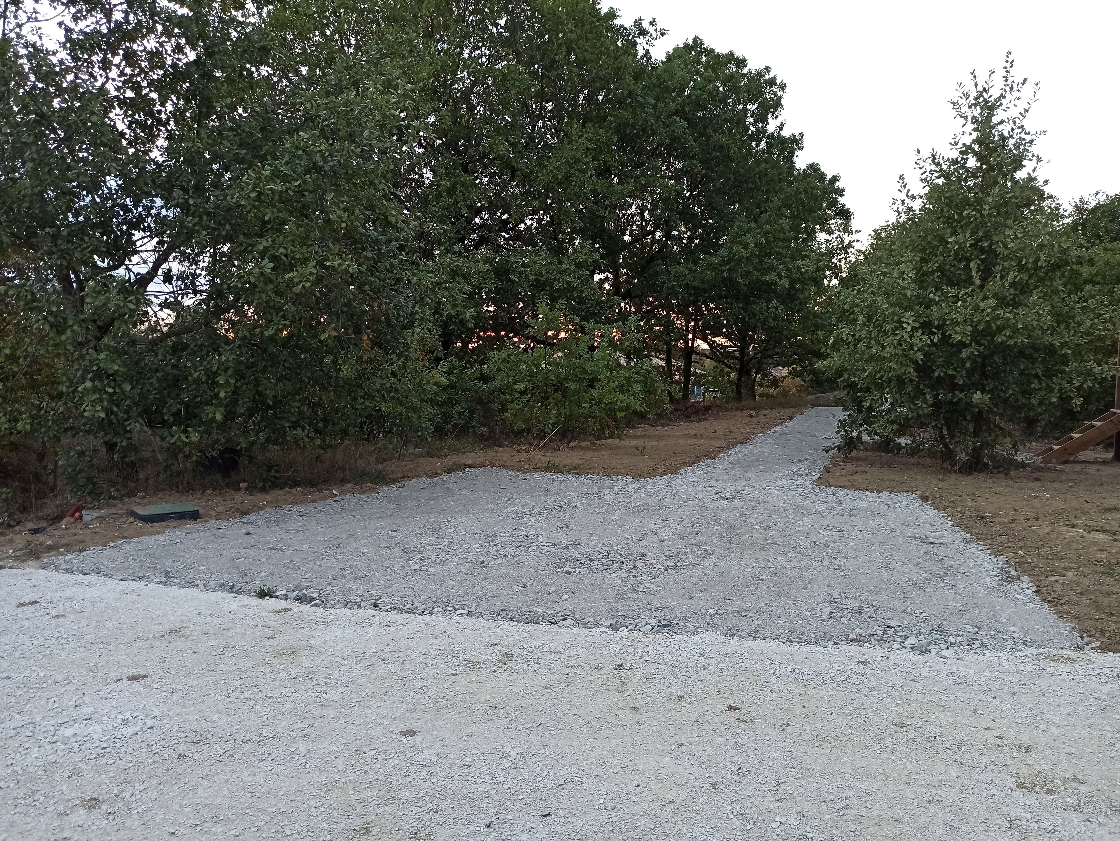 Ein Kiesweg führt durch ein bewaldetes Gebiet mit dichter Baumvegetation.