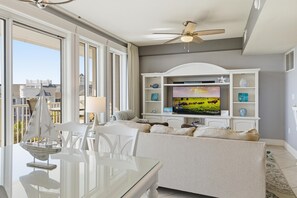 Ein Wohnzimmer mit Glastisch, weißem Sofa, Fernseher und Deckenventilator.