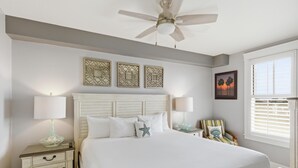 A bedroom with a bed, nightstands, a ceiling fan, wall art, and a window with blinds. - One Bedroom Condo at Grand Sandestin (Miramar Beach)