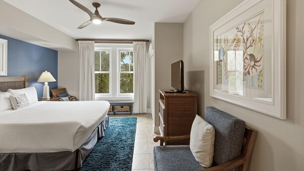 Ein Hotelzimmer mit einem Bett, einem Schreibtisch, einem Stuhl, einer Kommode, einem Deckenventilator und einem Fenster mit Vorhängen.