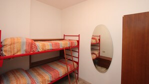 Une chambre avec des lits superposés, une armoire en bois et un miroir rond accroché au mur.
