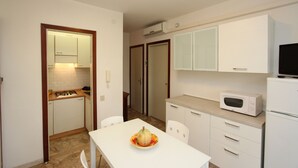 Une cuisine de taille réduite avec des meubles blancs, un four à micro-ondes et une table à manger avec des chaises.