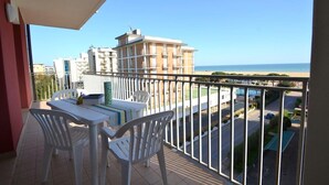 En balkon med bord og stole, udsigt over en strand og bygninger.