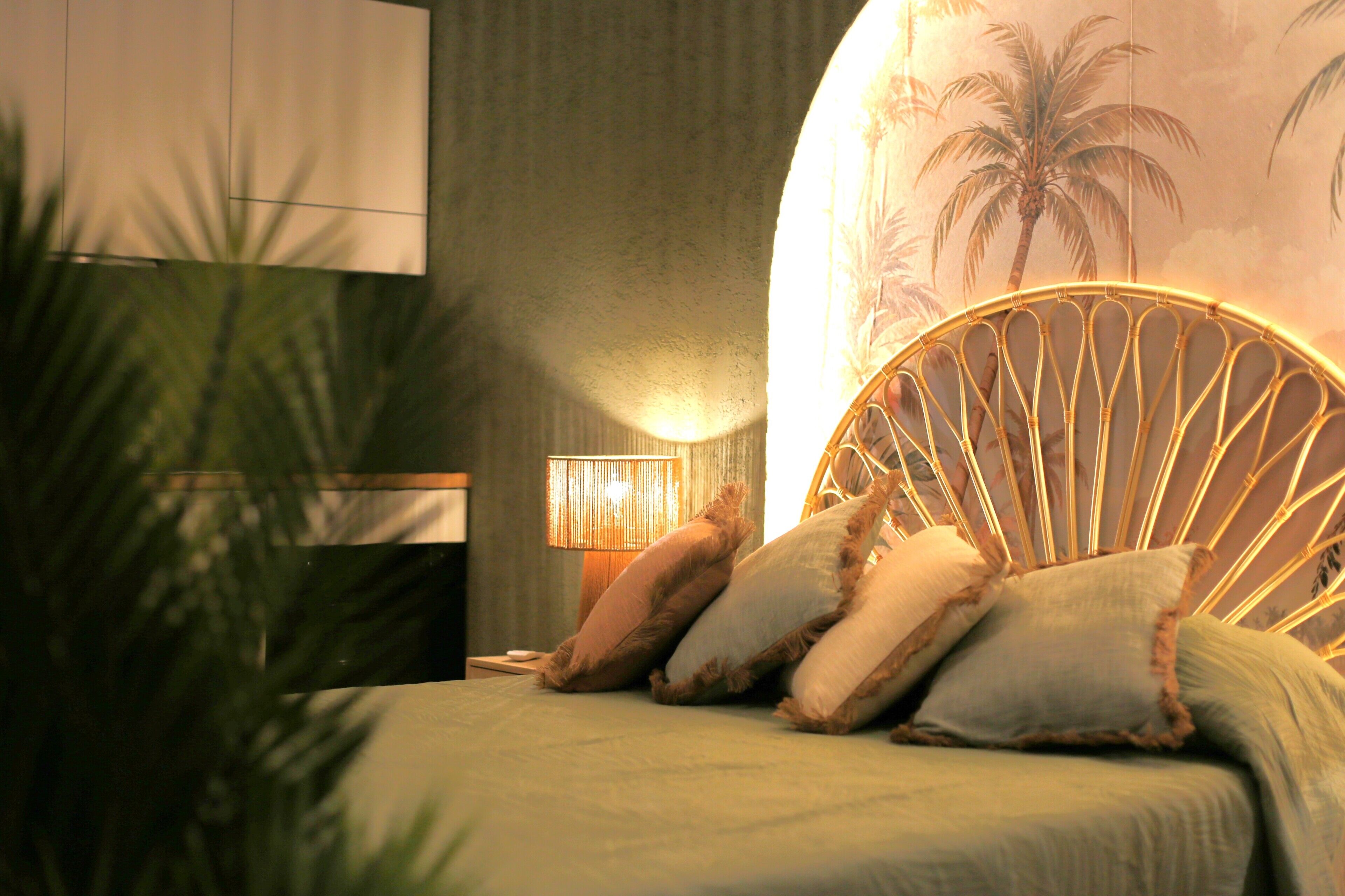 Een slaapkamer met een bed, nachtkastje, lamp en een muur met een palmboom muurschildering.