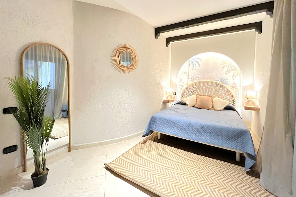 Une chambre à coucher comprenant un lit, un miroir, une plante en pot et un élément décoratif mural.
