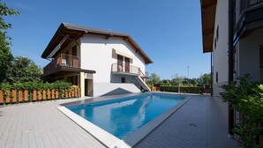 A two-story building with a swimming pool, a wooden fence, and a paved patio area.
