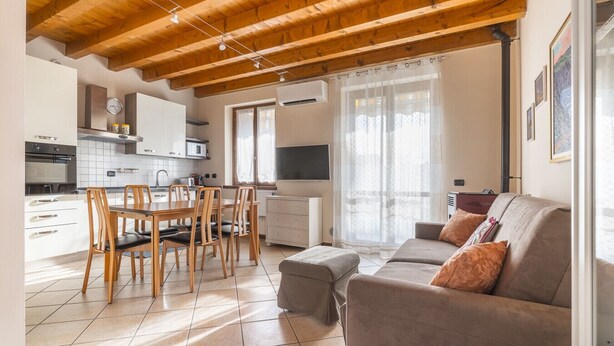A modern kitchen with white cabinets, a dining table with chairs, a sofa, and a TV.